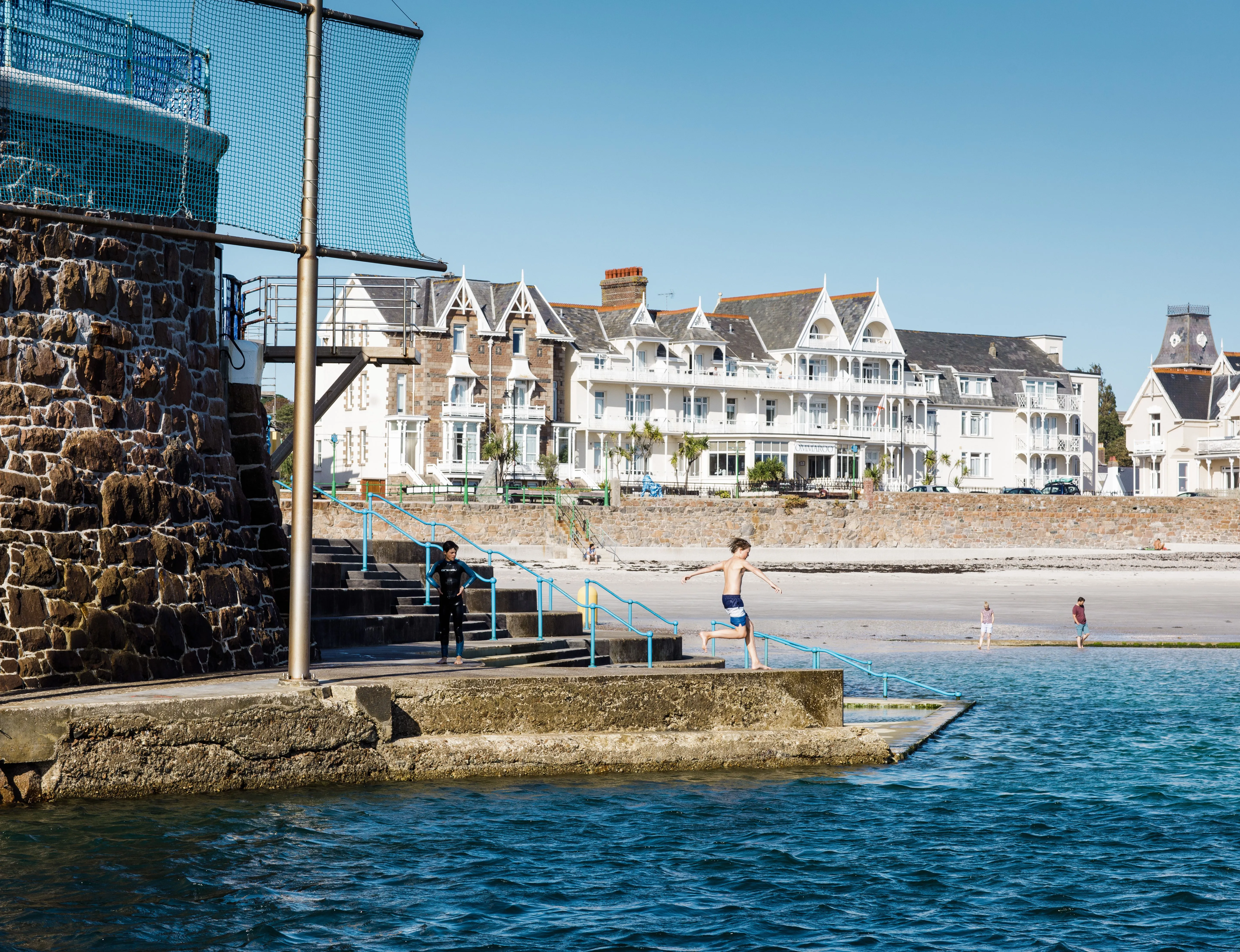 Boy jumping into the sea at Havre des Pas with beachfront buildings in the background