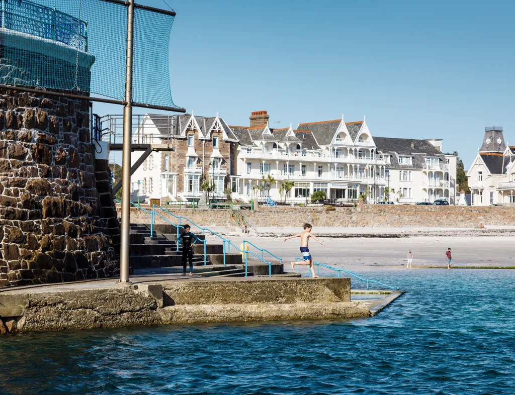 Boy jumping into the sea at Havre des Pas with beachfront buildings in the background
