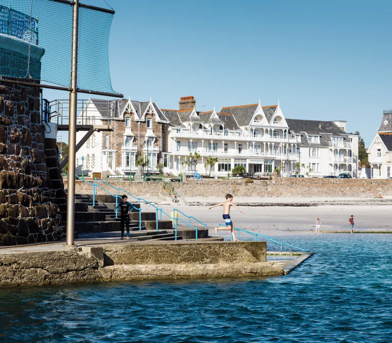 Boy jumping into the sea at Havre des Pas with beachfront buildings in the background