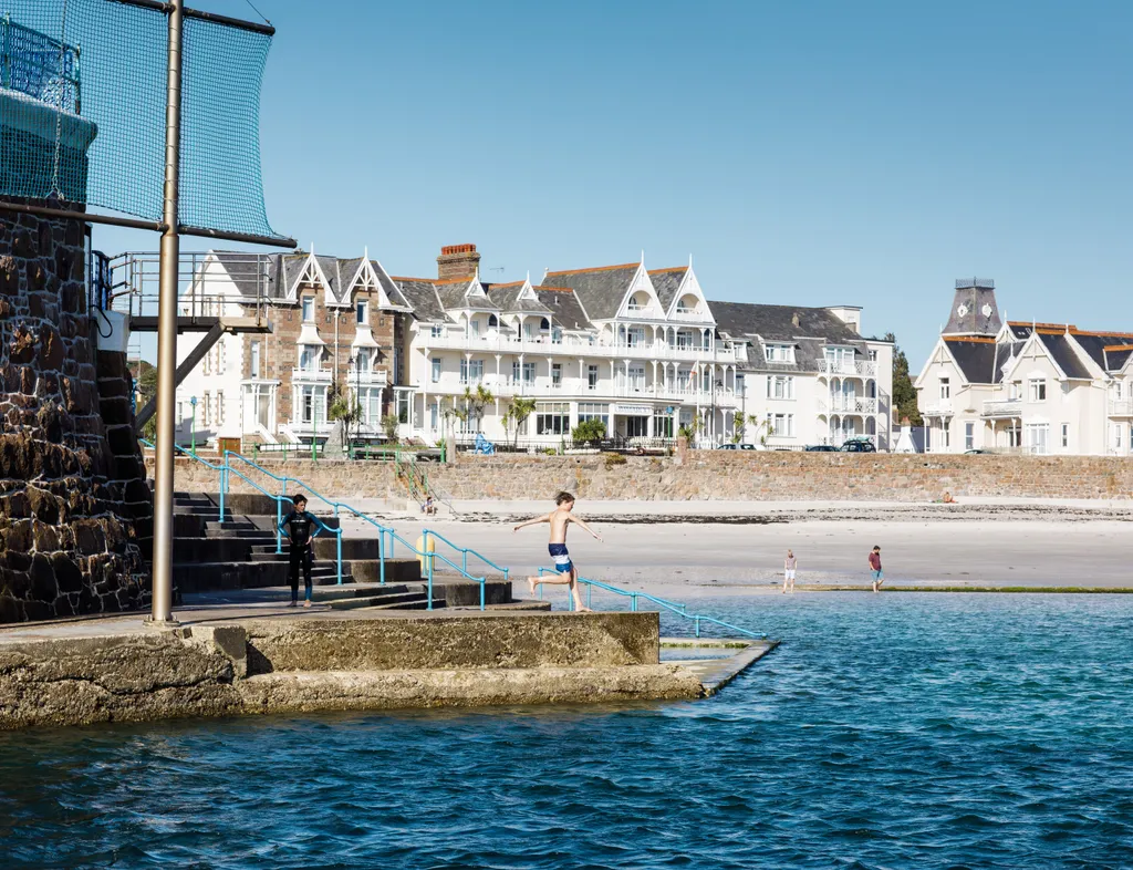 Boy jumping into the sea at Havre des Pas with beachfront buildings in the background