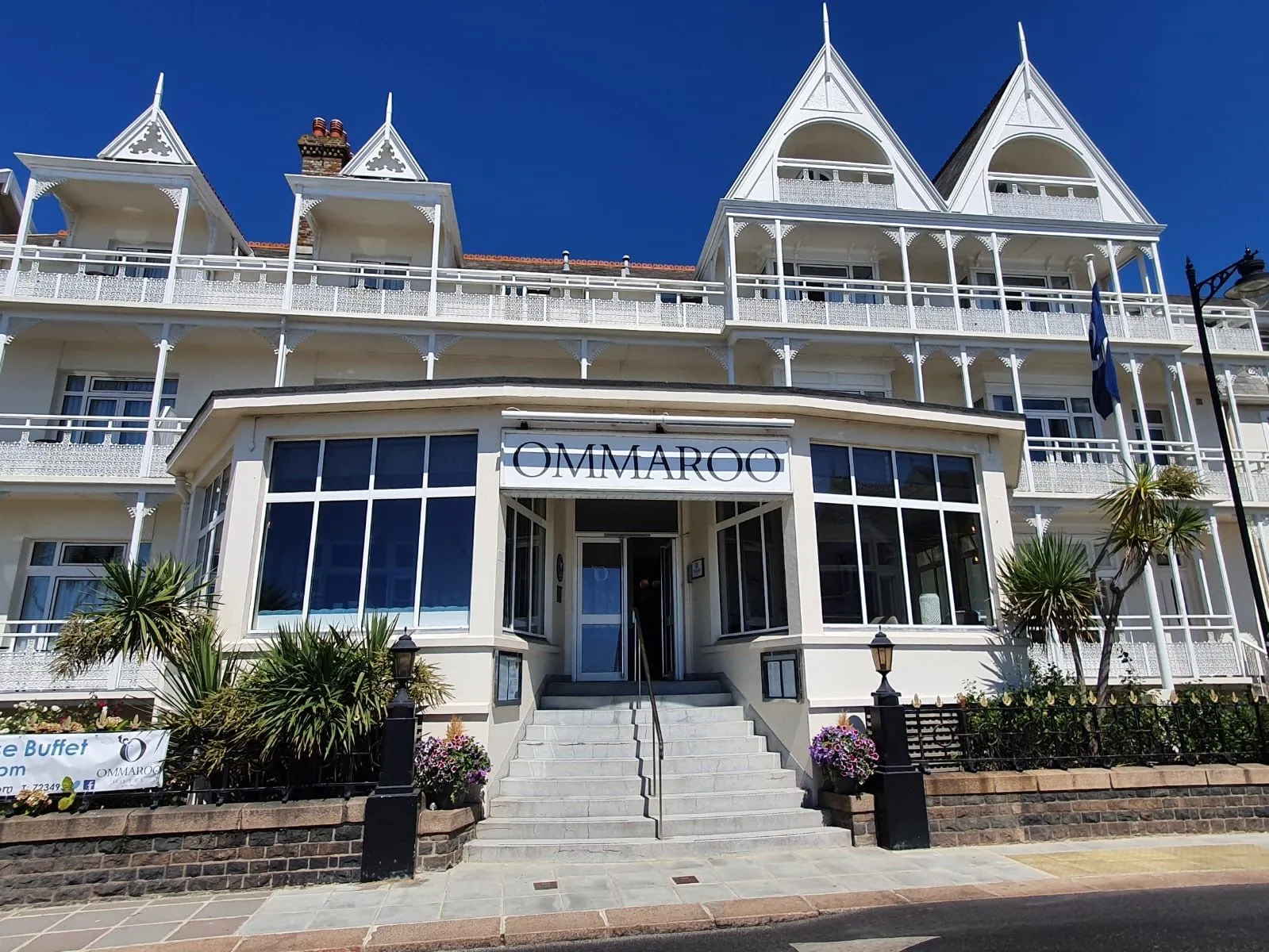 Front entrance of Ommaroo Hotel with white Victorian-style balconies and a bright blue sky