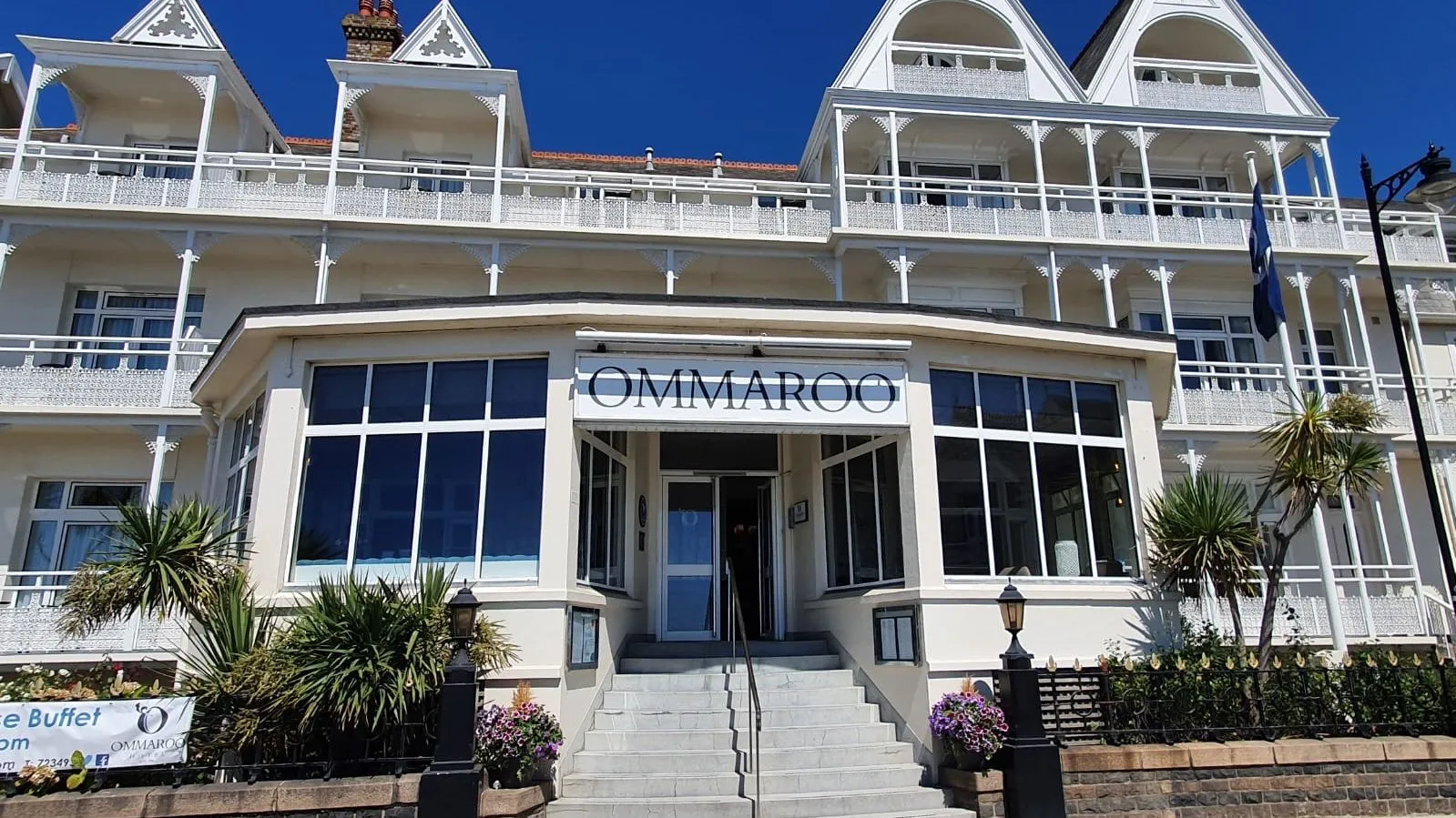 Front entrance of Ommaroo Hotel with white Victorian-style balconies and a bright blue sky