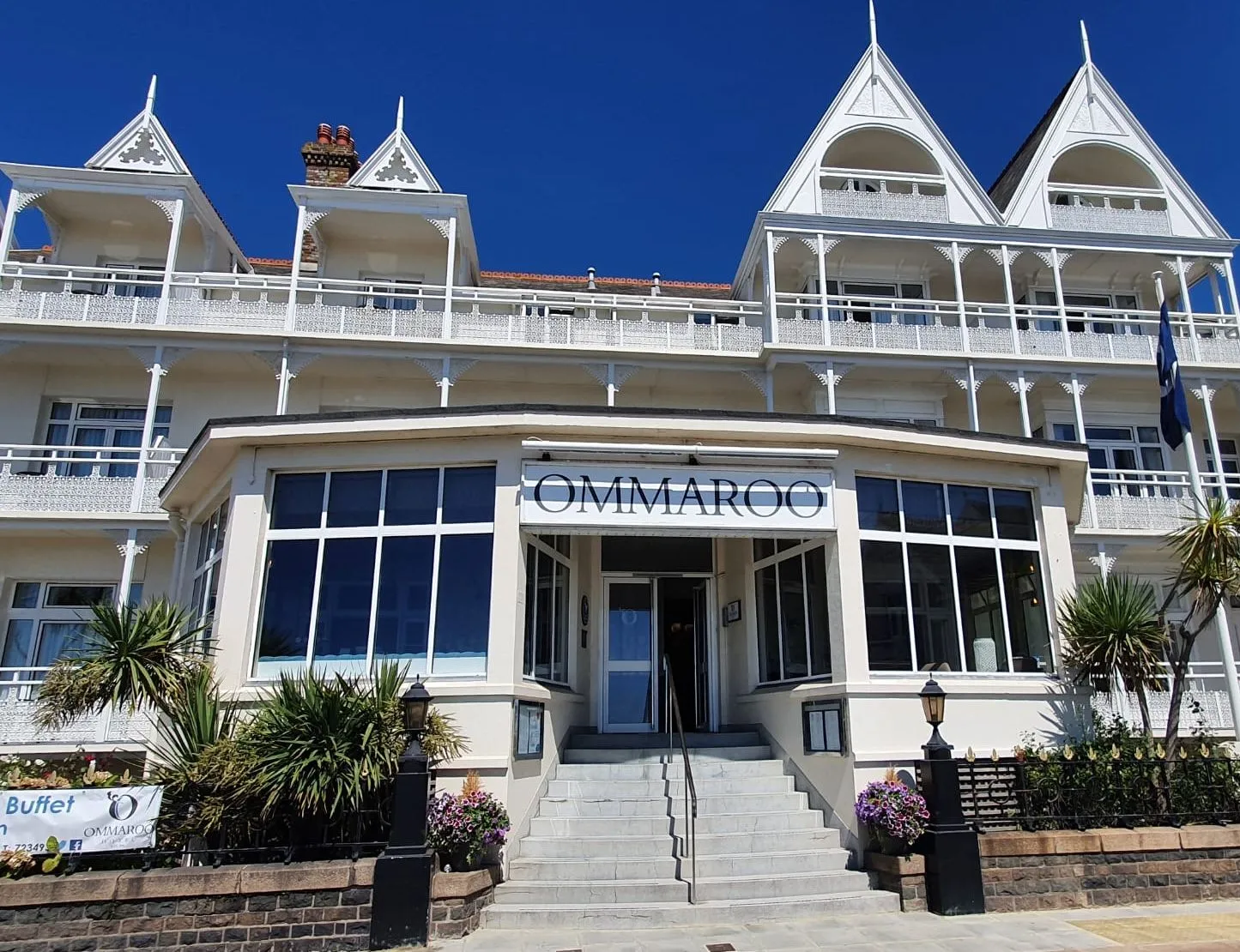 Front entrance of Ommaroo Hotel with white Victorian-style balconies and a bright blue sky