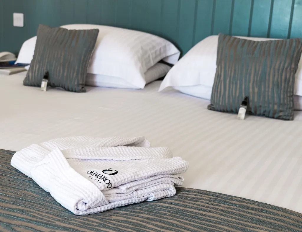 Spacious hotel bed with crisp white linen, teal cushions and folded bathrobes in a seaview balcony room