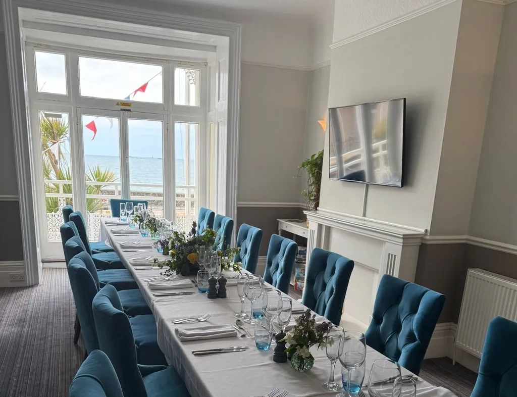 Long dining table set in a seaview lounge with blue upholstered chairs and large windows overlooking the sea