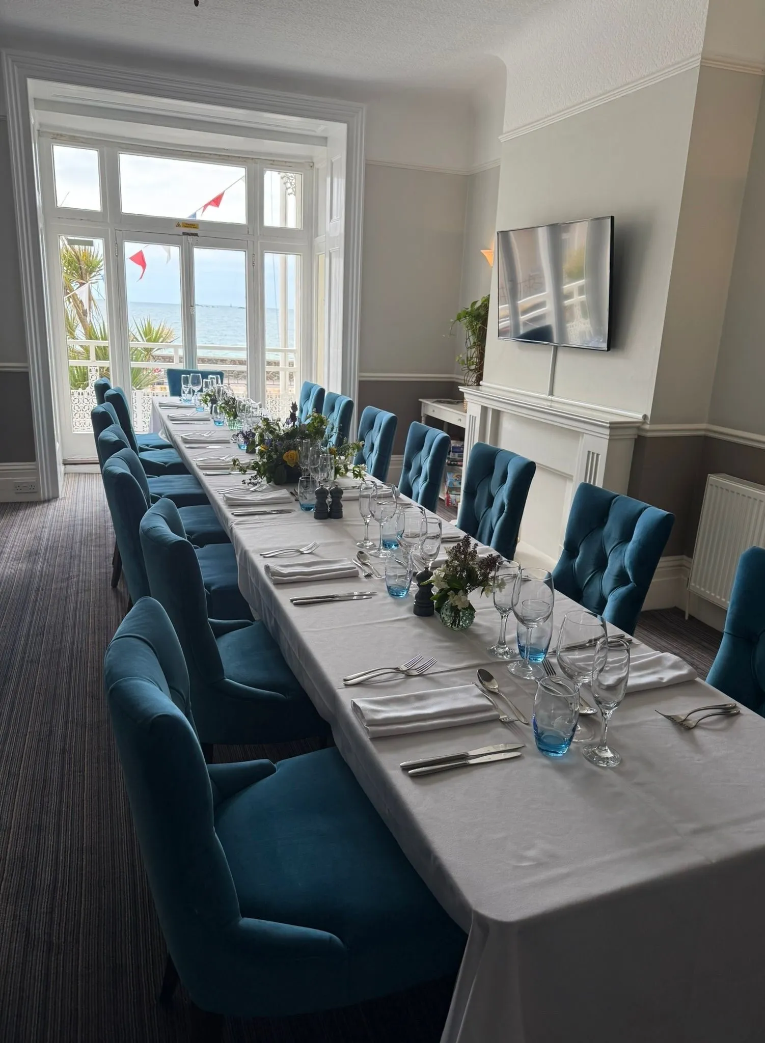 Long dining table set in a seaview lounge with blue upholstered chairs and large windows overlooking the sea