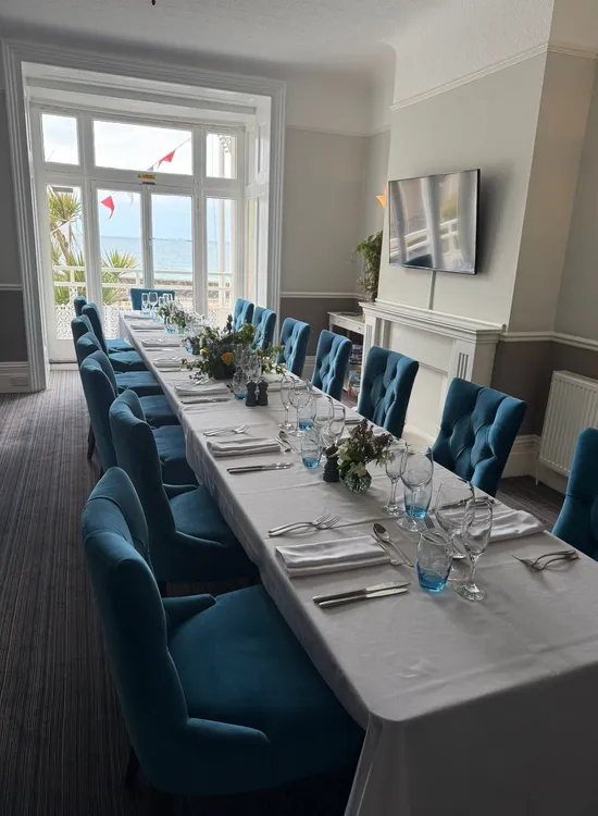 Long dining table set in a seaview lounge with blue upholstered chairs and large windows overlooking the sea