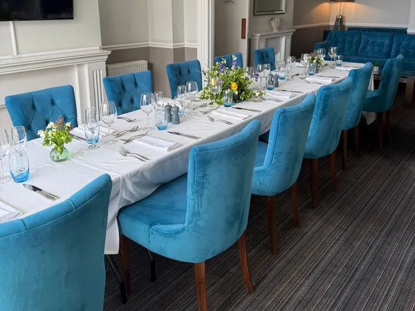 Elegant seaview lounge dining room with a long table set for dinner, blue upholstered chairs and floral centrepieces.