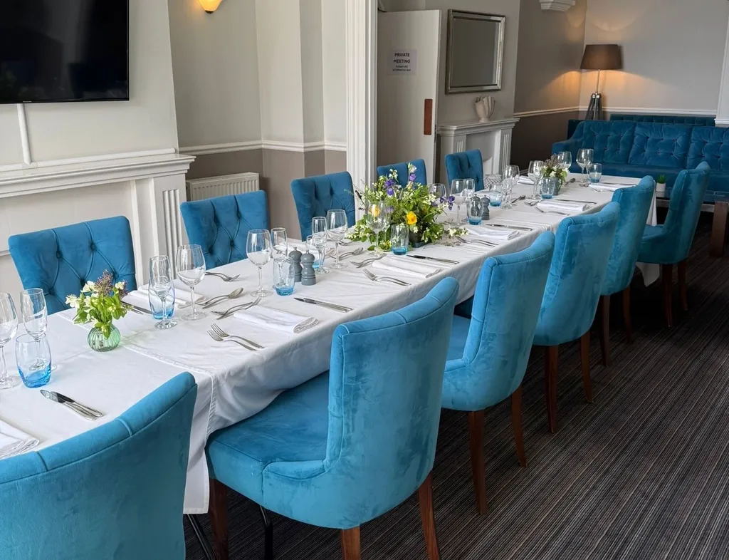 Elegant seaview lounge dining room with a long table set for dinner, blue upholstered chairs and floral centrepieces.