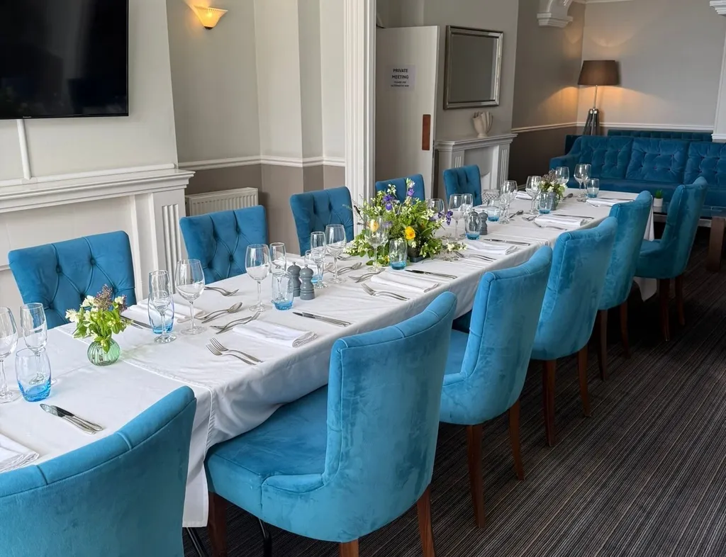 Elegant seaview lounge dining room with a long table set for dinner, blue upholstered chairs and floral centrepieces.