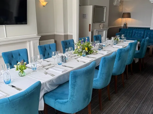 Elegant seaview lounge dining room with a long table set for dinner, blue upholstered chairs and floral centrepieces.