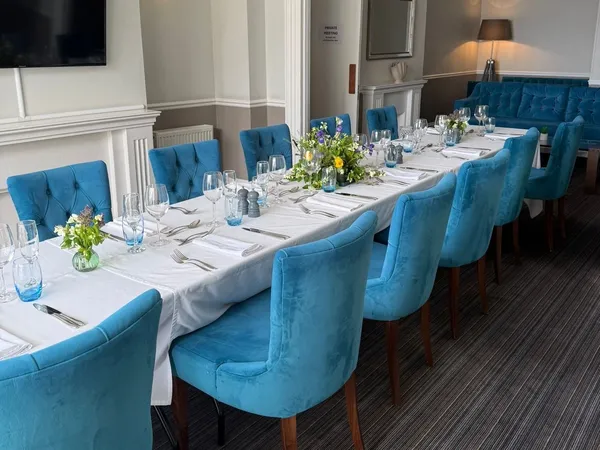 Elegant seaview lounge dining room with a long table set for dinner, blue upholstered chairs and floral centrepieces.