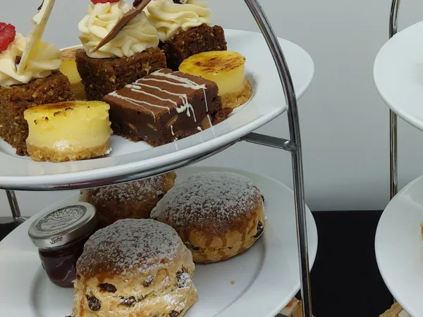 Three-tier afternoon tea stand with finger sandwiches, fruit scones with jam, and assorted miniature cakes and desserts.