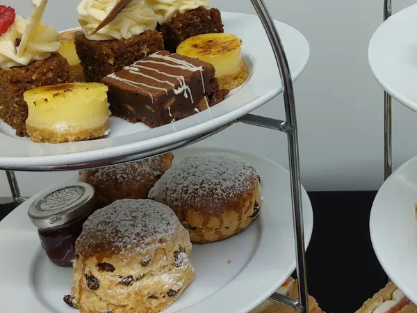 Three-tier afternoon tea stand with finger sandwiches, fruit scones with jam, and assorted miniature cakes and desserts.