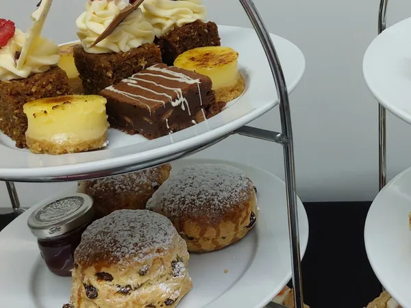 Three-tier afternoon tea stand with finger sandwiches, fruit scones with jam, and assorted miniature cakes and desserts.