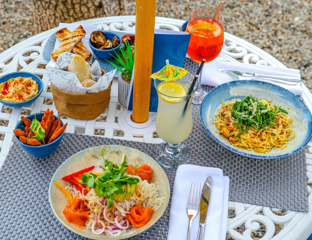Outdoor terrace dining table with pasta, smoked salmon noodle salad, bread, dips, sweet potato wedges and cocktails.