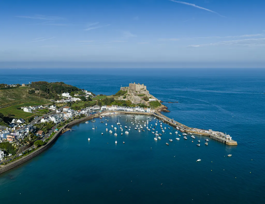 Aerial view of Gorey Harbour and Mont Orgueil Castle on the Jersey coastline under a clear blue sky.