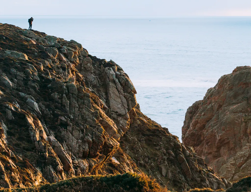 Photographer standing on a rocky coastal cliff overlooking the sea