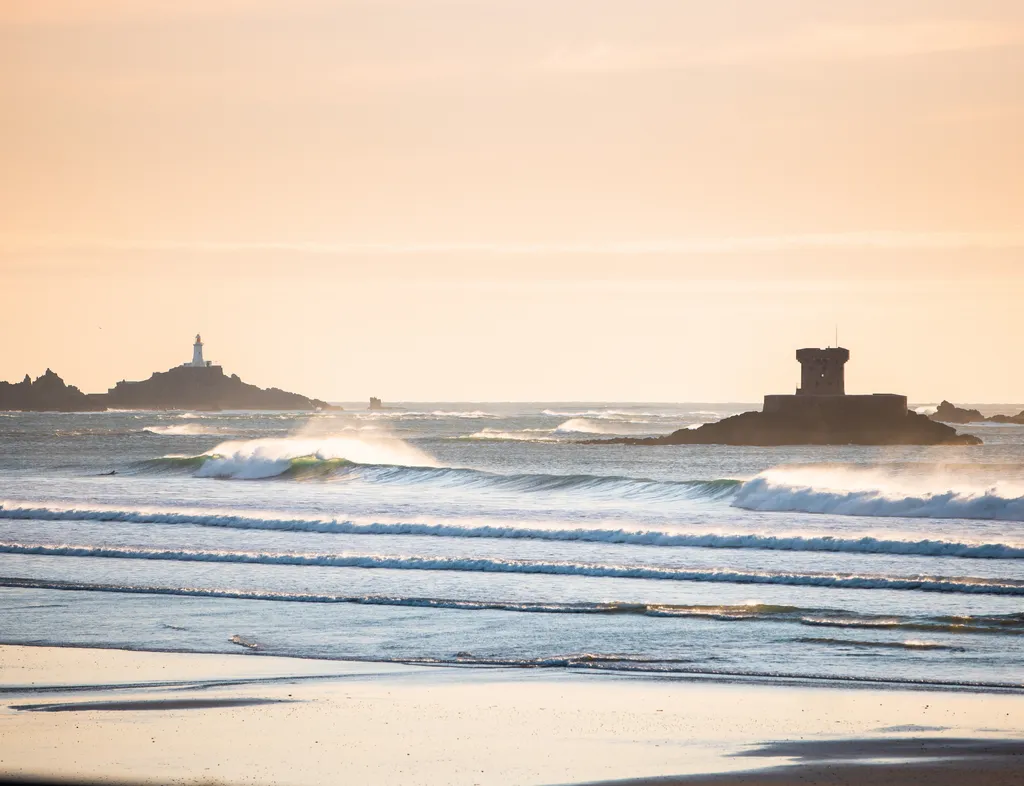 Golden seascape with rolling waves, a coastal tower on a rocky islet, and a lighthouse in the distance