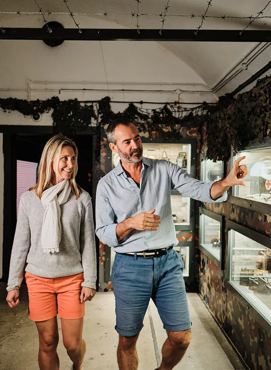 A man and woman walking through a military museum corridor, looking at wartime displays in illuminated cases.