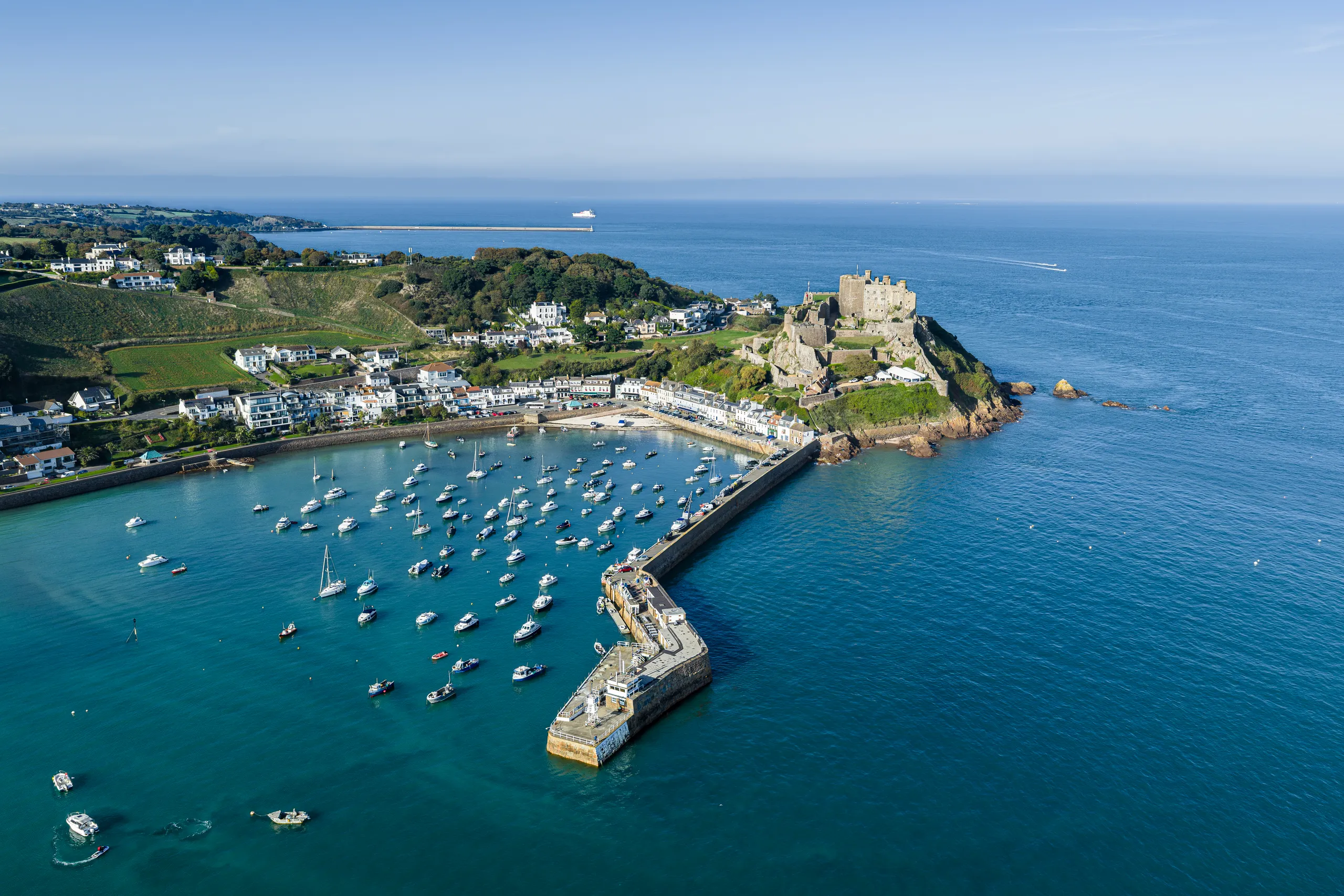 Aerial view of Gorey Harbour and Mont Orgueil Castle in Jersey, with boats moored inside the harbour and the sea stretching beyond.