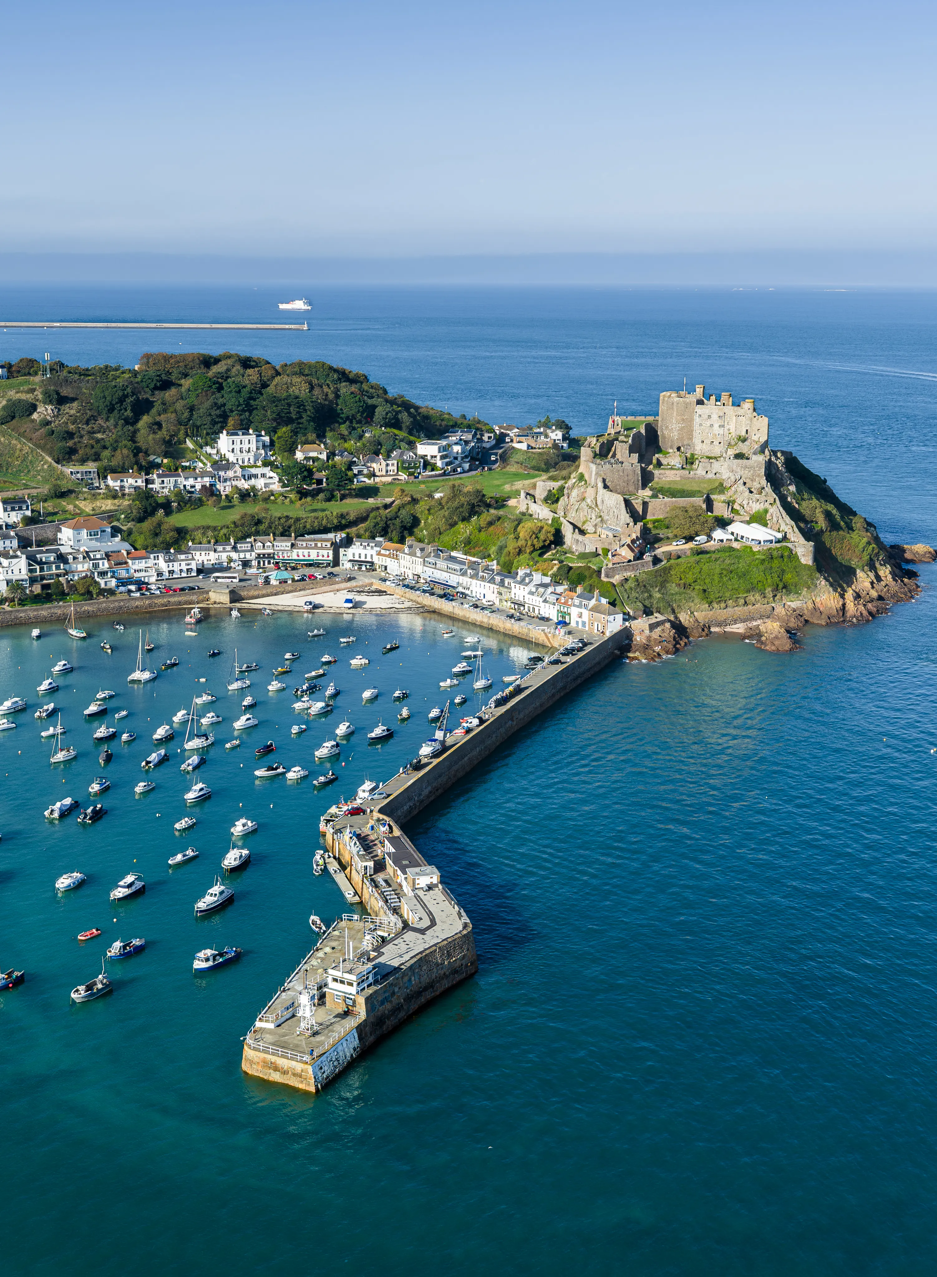 Aerial view of Gorey Harbour and Mont Orgueil Castle in Jersey, with boats moored inside the harbour and the sea stretching beyond.