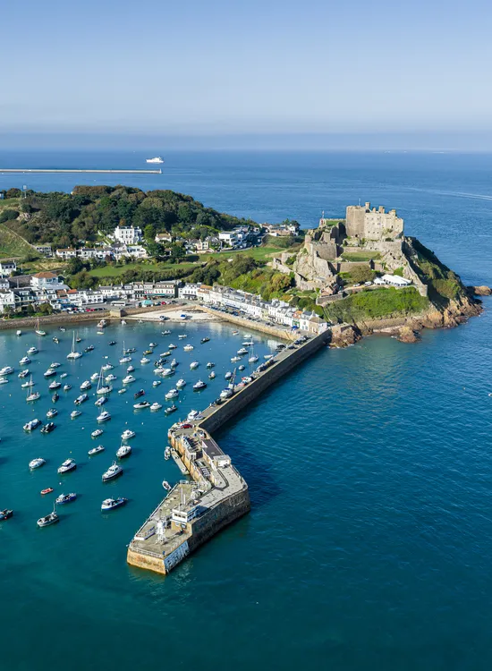 Aerial view of Gorey Harbour and Mont Orgueil Castle in Jersey, with boats moored inside the harbour and the sea stretching beyond.