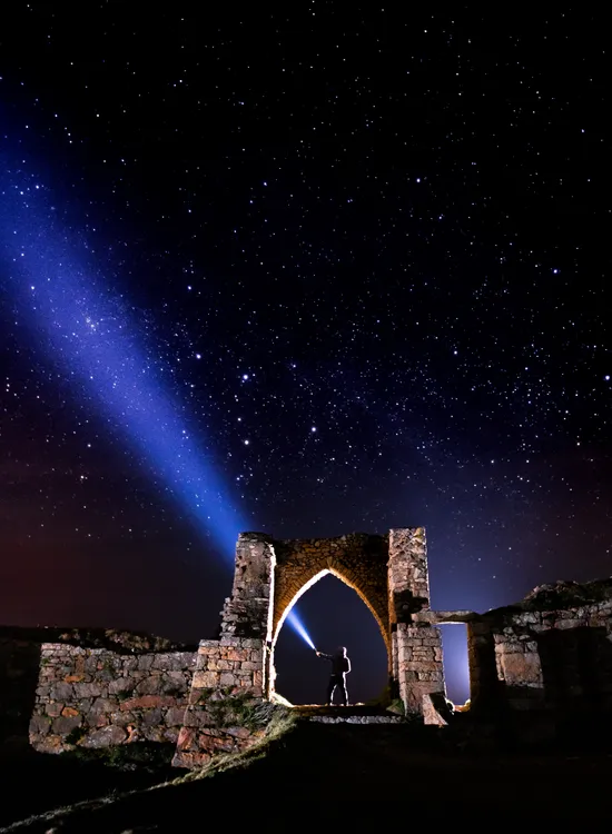 Silhouette of a person shining a torch through a stone archway beneath a star-filled night sky