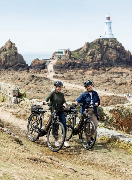 Two women with bicycles on a coastal path near Corbière Lighthouse, Jersey