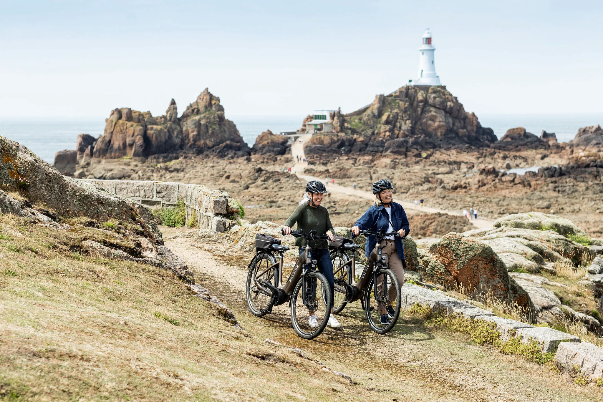 Two women with bicycles on a coastal path near Corbière Lighthouse, Jersey