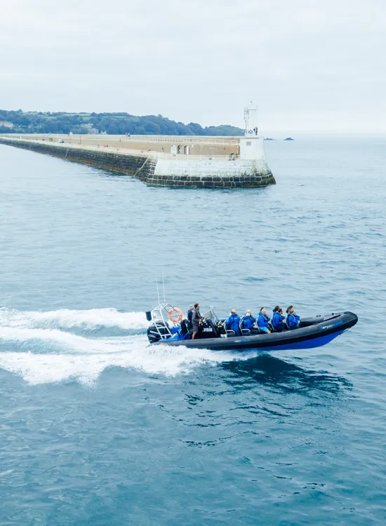 Rigid inflatable boat speeding across calm blue water near a long harbour breakwater