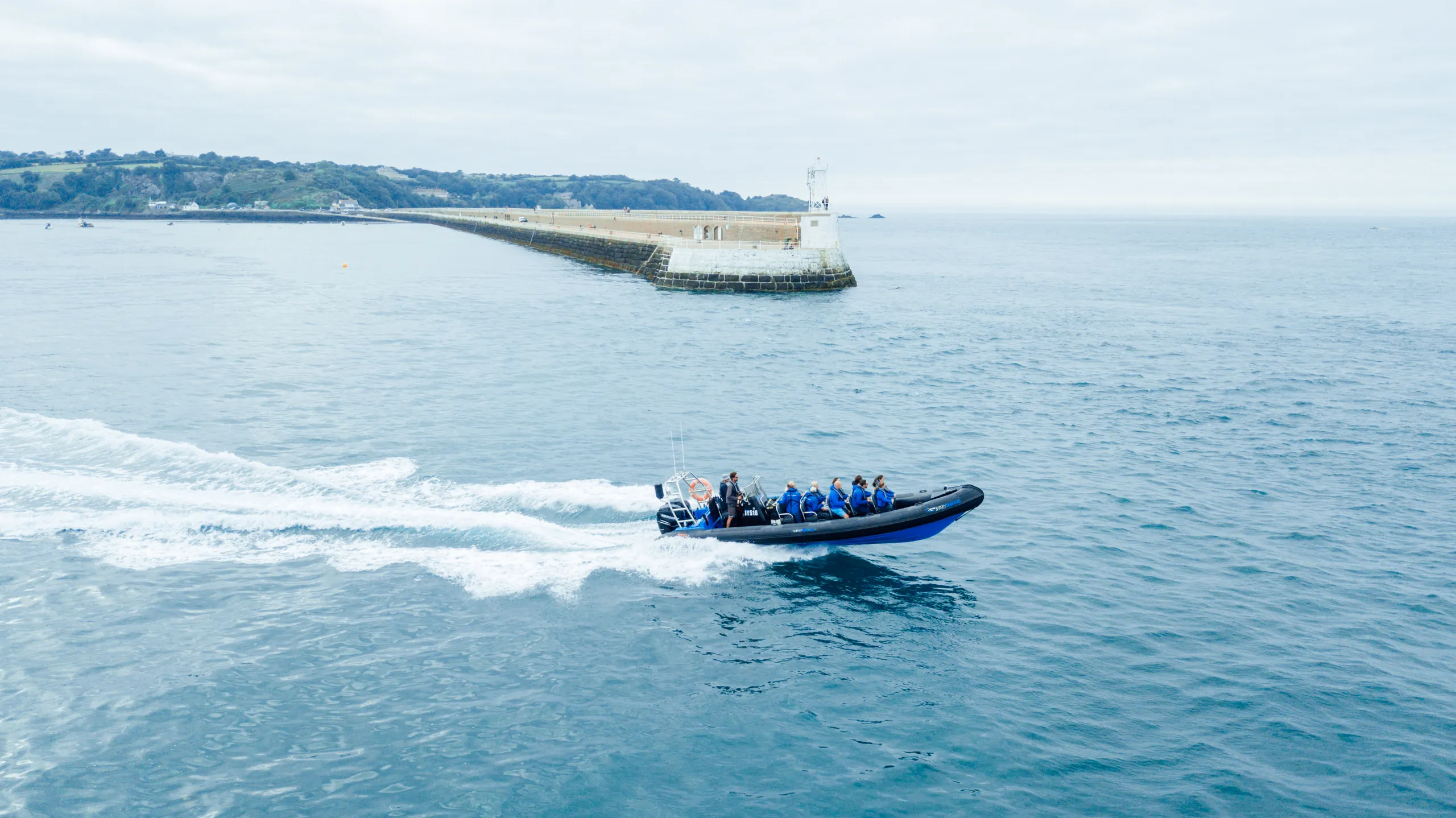 Rigid inflatable boat speeding across calm blue water near a long harbour breakwater