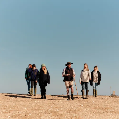 Group of walkers crossing a wide sandy shore on the Seymour Trail in Jersey under a clear blue sky.