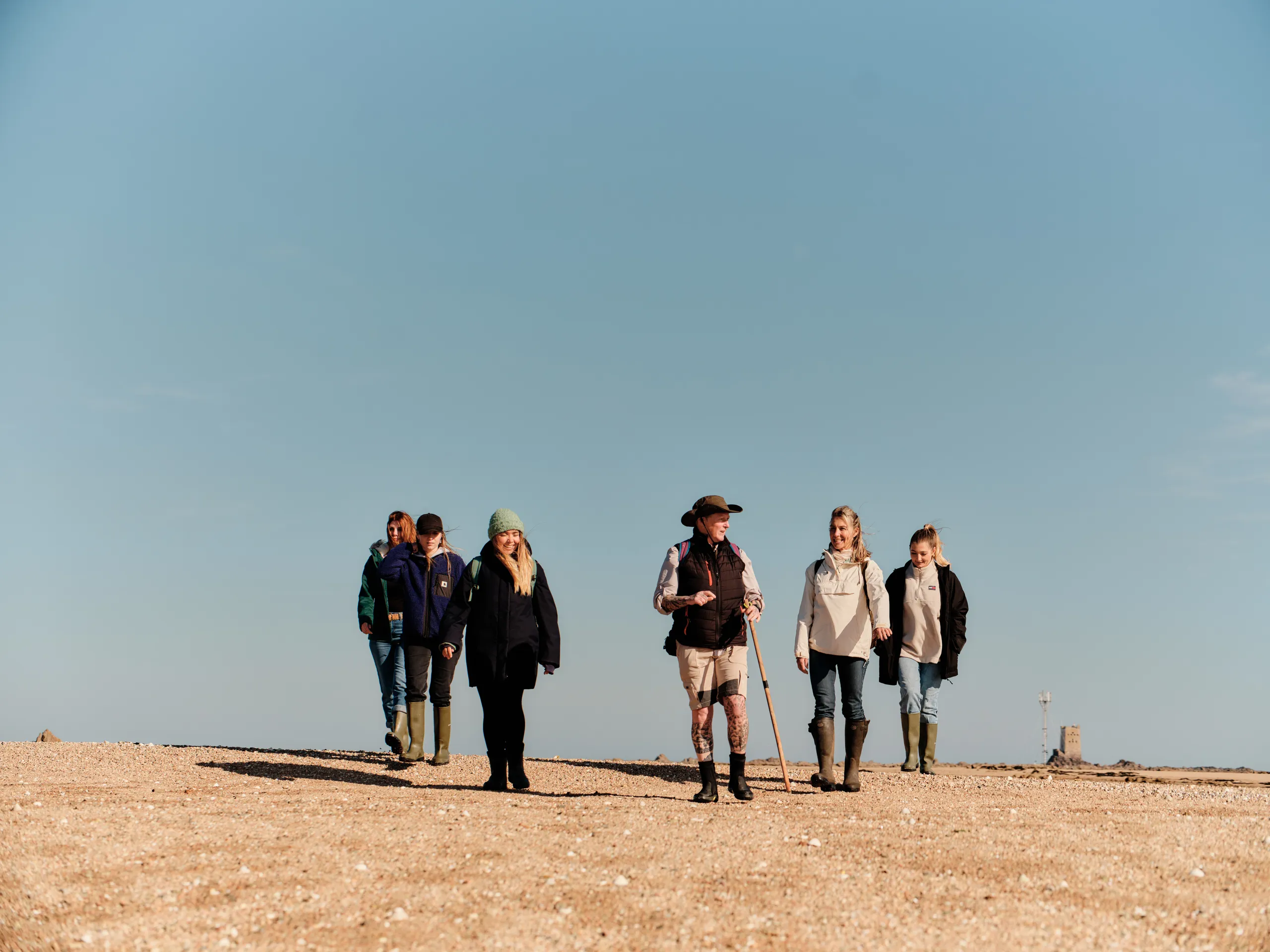 Group of walkers crossing a wide sandy shore on the Seymour Trail in Jersey under a clear blue sky.