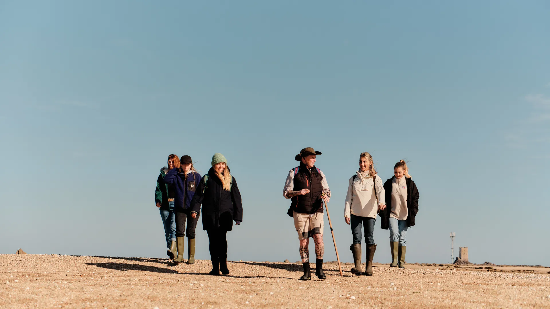 Group of walkers crossing a wide sandy shore on the Seymour Trail in Jersey under a clear blue sky.