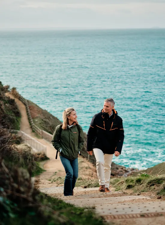 Couple walking up the coastal path at Devil's Hole in Jersey with the sea behind them