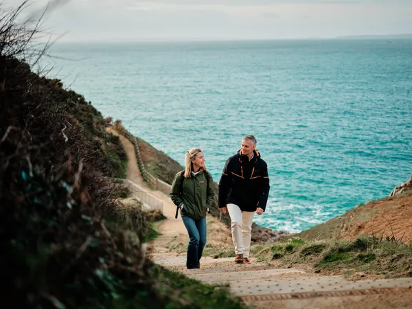 Couple walking up the coastal path at Devil's Hole in Jersey with the sea behind them