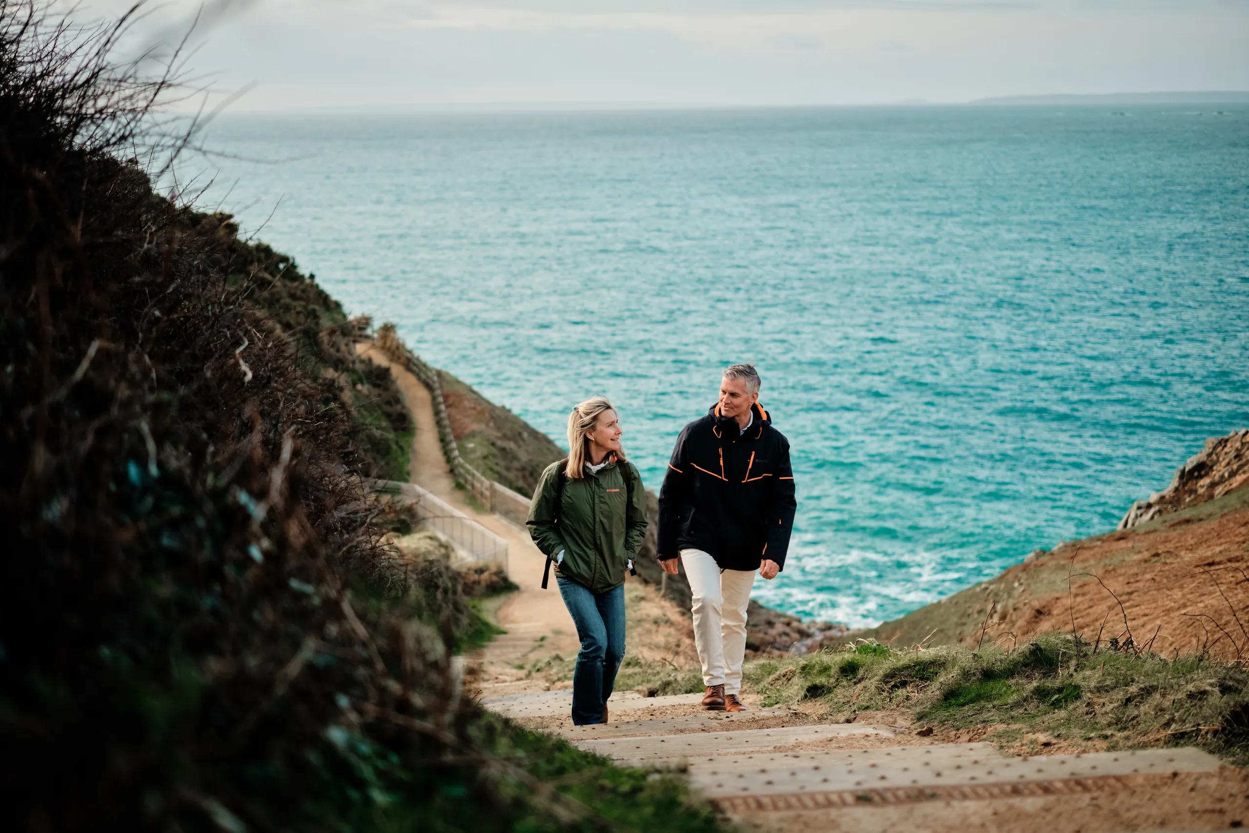 Couple walking up the coastal path at Devil's Hole in Jersey with the sea behind them