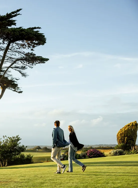 Couple walking across the lawn beside wind-shaped coastal trees at Atlantic Hotel