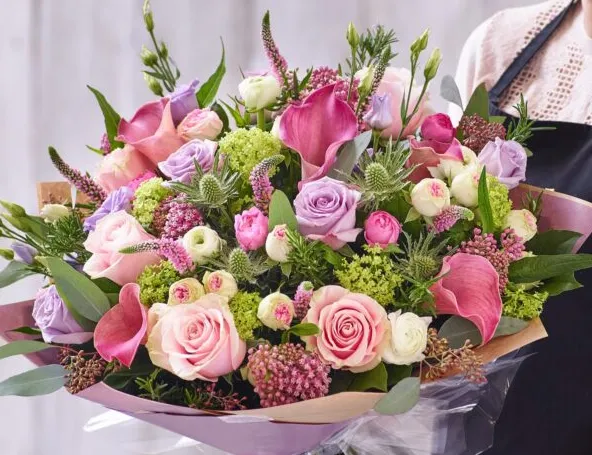 Large hand-tied bouquet of pink calla lilies, roses and pastel flowers wrapped in paper and cellophane