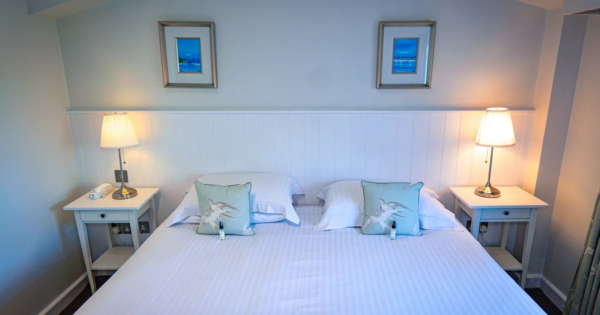 Classic room with a neatly made double bed, matching bedside tables, lamps, and framed coastal artwork.