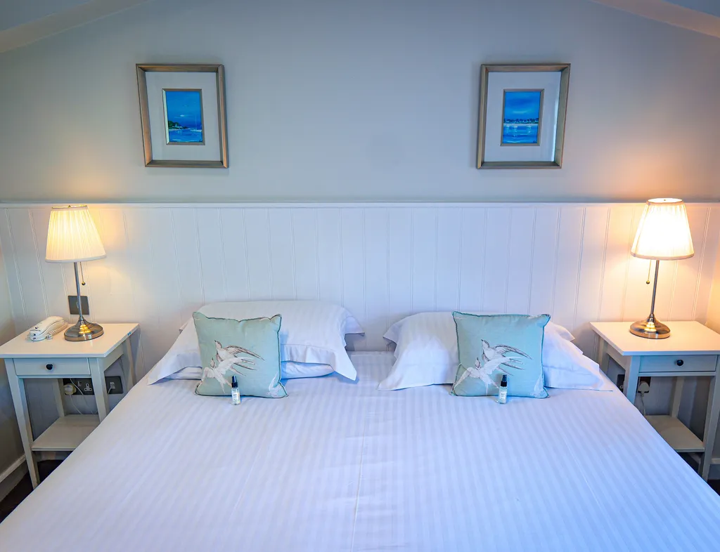 Classic room with a neatly made double bed, matching bedside tables, lamps, and framed coastal artwork.