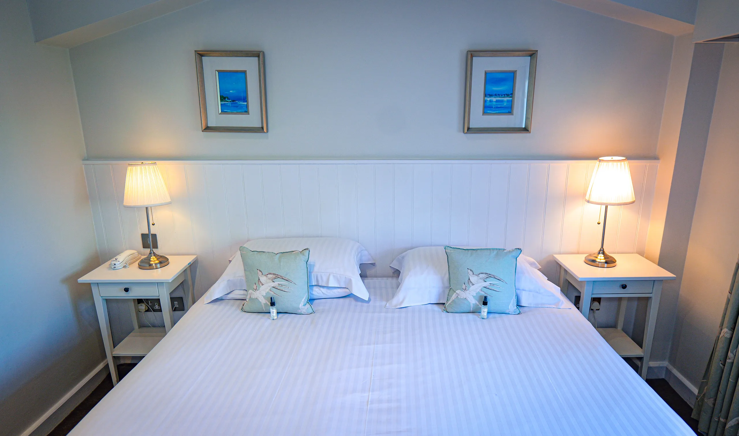 Classic room with a neatly made double bed, matching bedside tables, lamps, and framed coastal artwork.