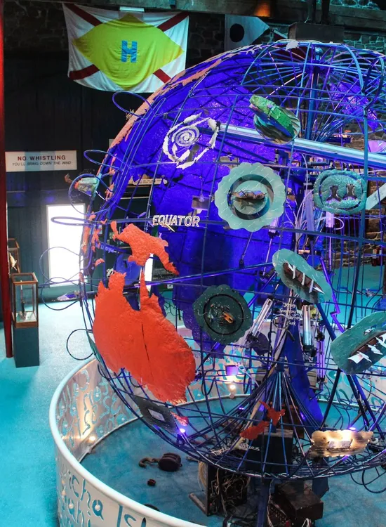 Large illuminated globe installation inside a maritime museum with colourful displays and nautical flags overhead.