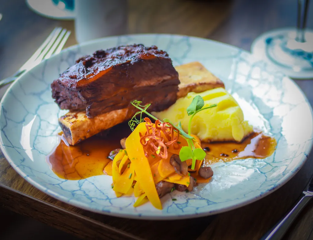 Braised beef short rib served with mashed potato, roasted bone marrow, carrots and rich gravy on a marbled plate