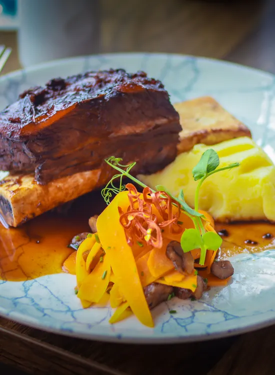 Braised beef short rib served with mashed potato, roasted bone marrow, carrots and rich gravy on a marbled plate