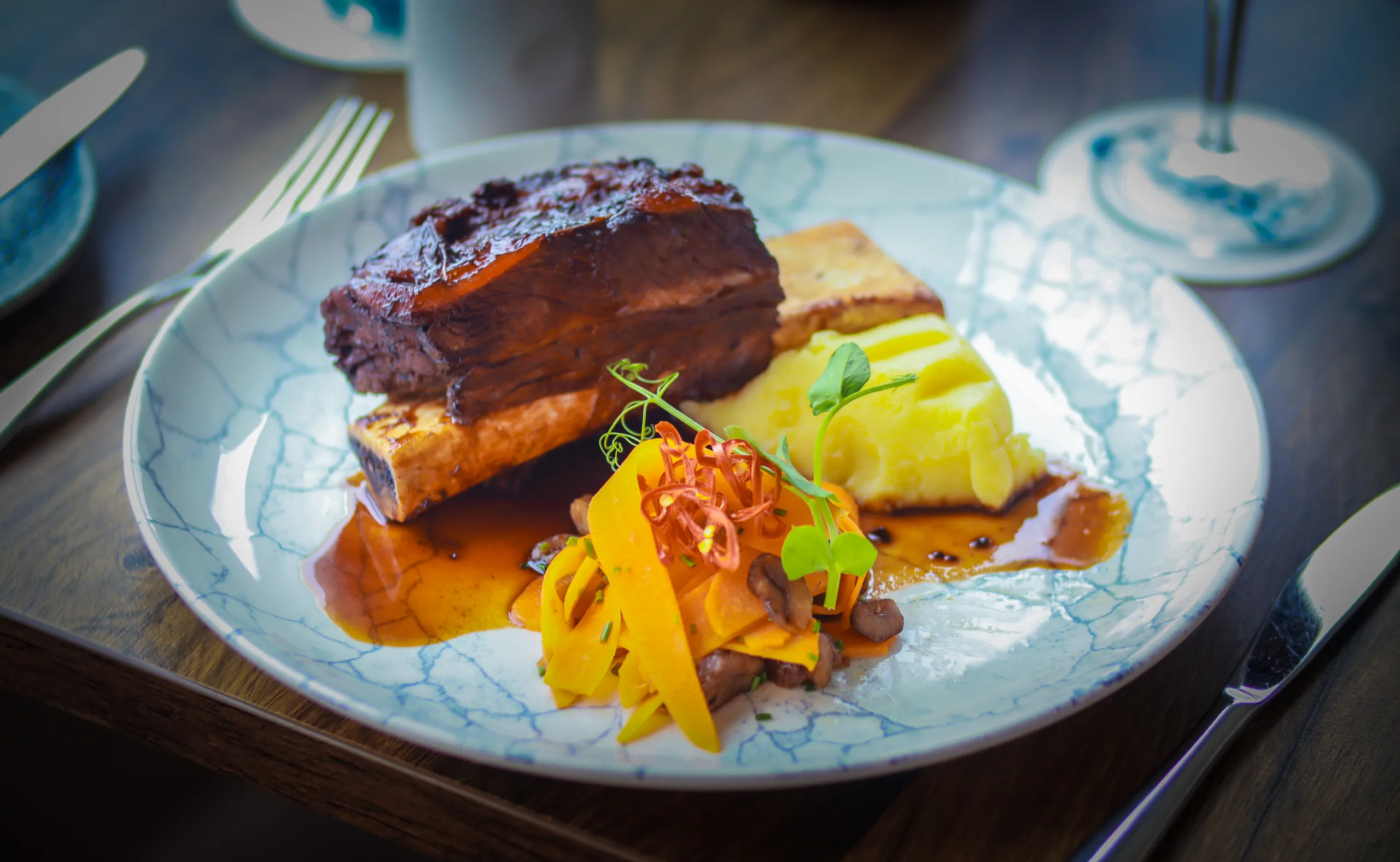 Braised beef short rib served with mashed potato, roasted bone marrow, carrots and rich gravy on a marbled plate