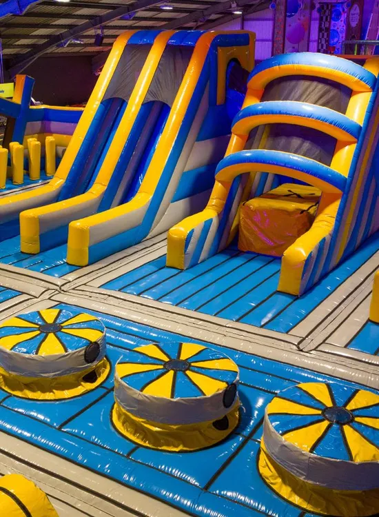 Blue and yellow inflatable jump jersey obstacle course with slides inside an indoor activity park