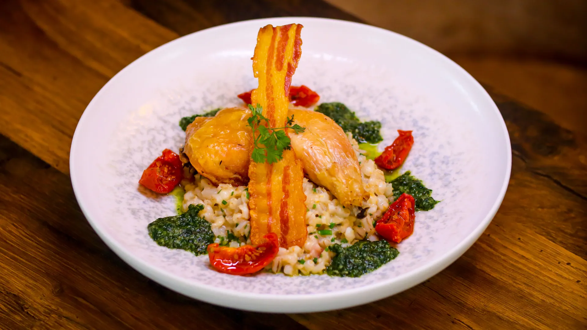 Roast chicken served on creamy risotto with crispy bacon, roasted tomatoes and green herb sauce