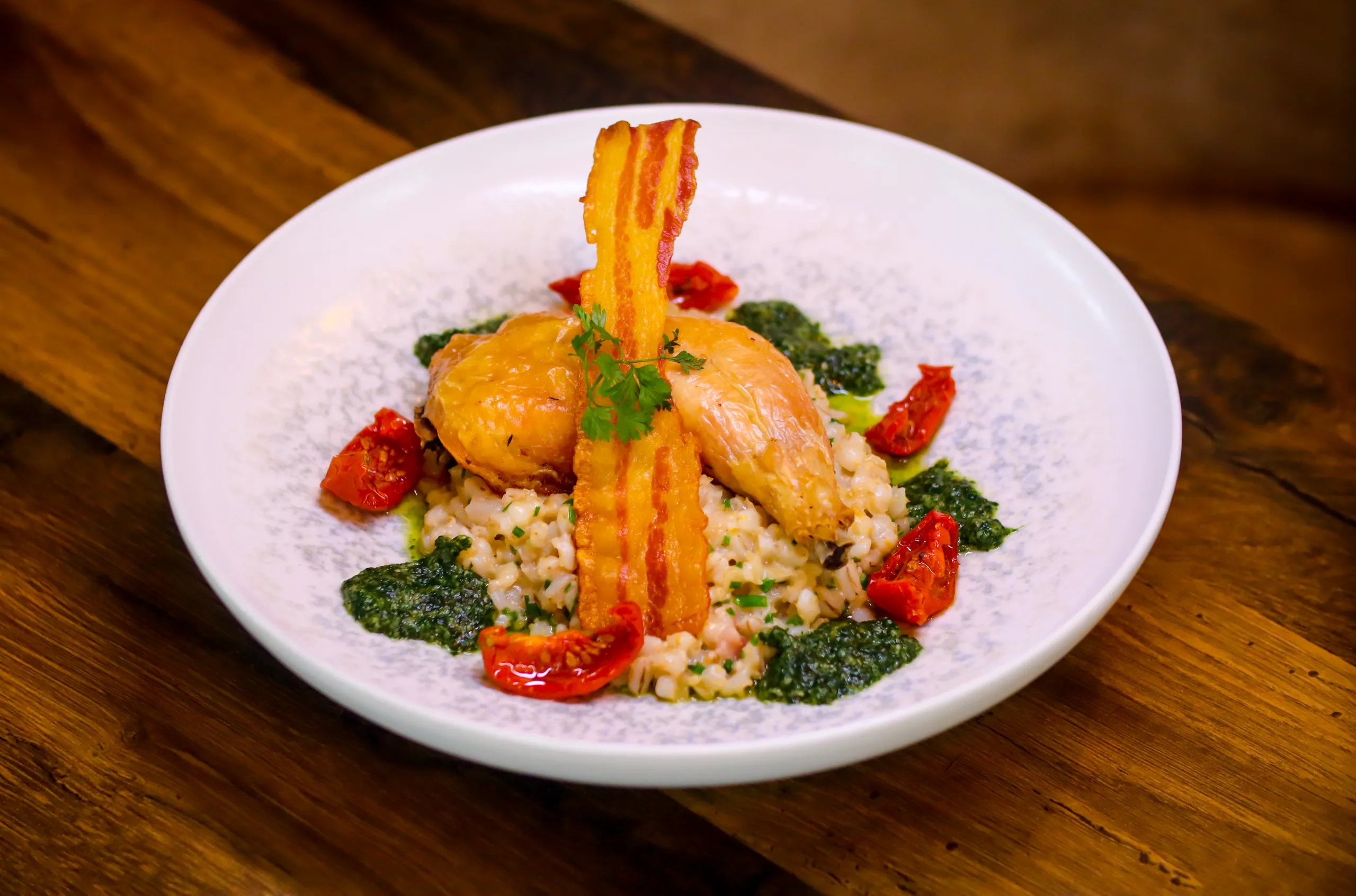 Roast chicken served on creamy risotto with crispy bacon, roasted tomatoes and green herb sauce